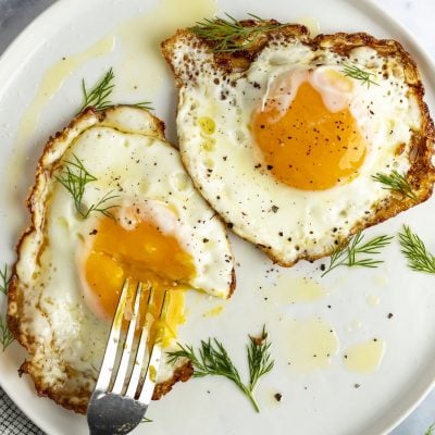 2 crispy fried eggs on white plate with fork poking into runny yolk