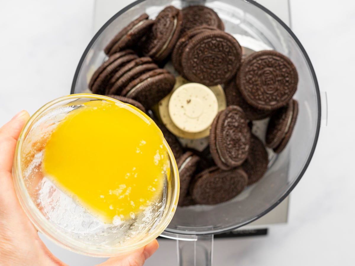 pouring melted butter into food processor filled with oreos.