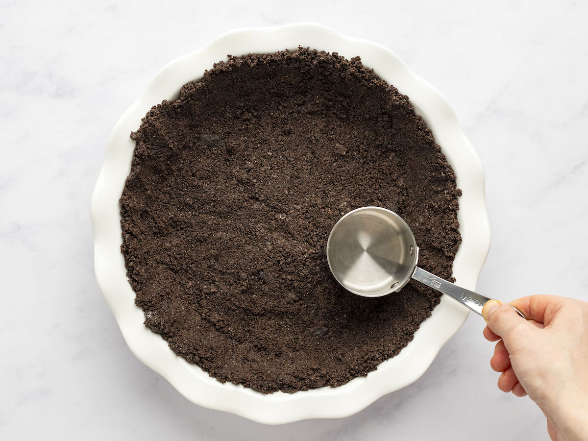 pressing the crumbs to form the Oreo crust.