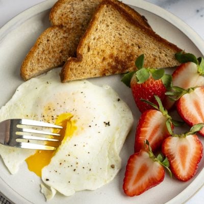 over easy egg, strawberries and toast on white plate with fork in runny yolk