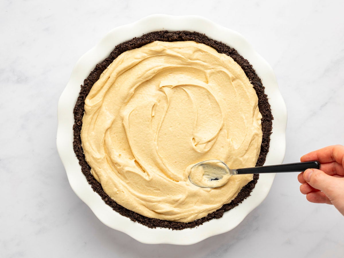 assembling peanut butter pie, spreading the filling into the Oreo crust.