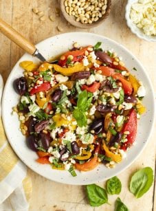 roasted pepper salad in white bowl with basil, pine nuts, olives, and feta cheese.