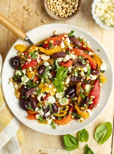 roasted pepper salad in white bowl with basil, pine nuts, olives, and feta cheese.