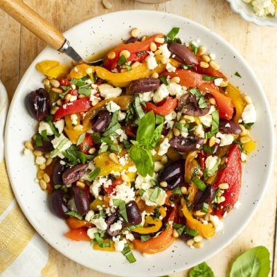 roasted pepper salad in white bowl with basil, pine nuts, olives, and feta cheese.