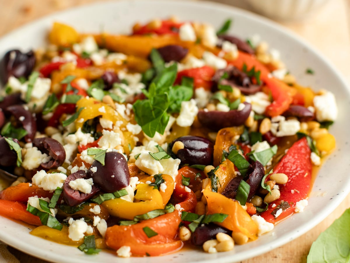 roasted pepper salad in white bowl with basil, pine nuts, olives, and feta cheese.
