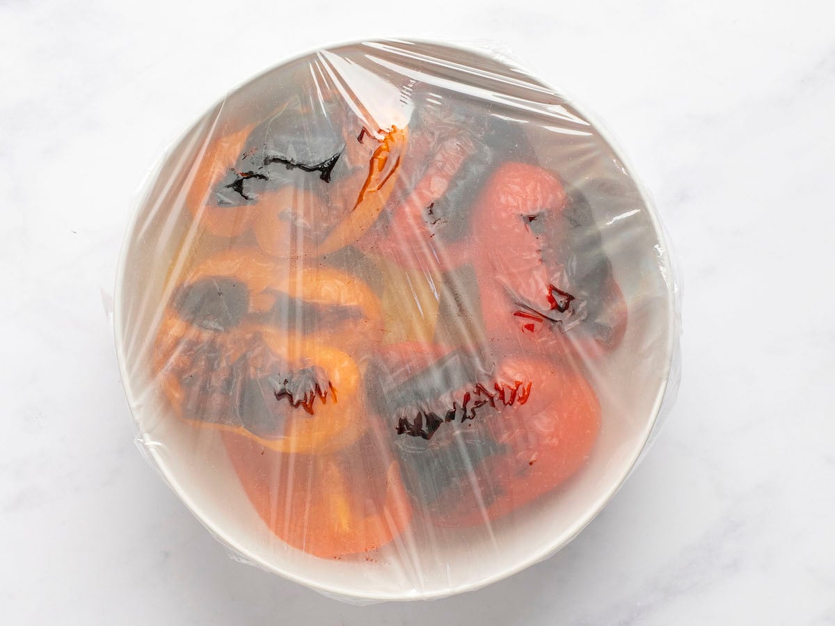 roasted peppers steaming in bowl covered with plastic wrap.