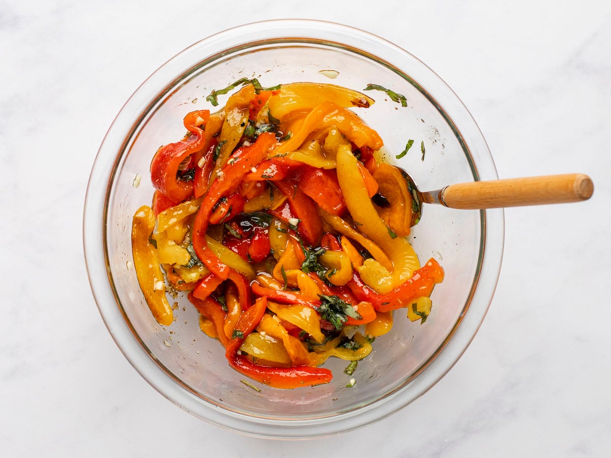 tossing roasted pepper salad in bowl with spoon.