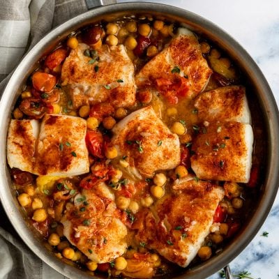 baked cod with tomatoes and chickpeas in skillet with plaid linen napkin