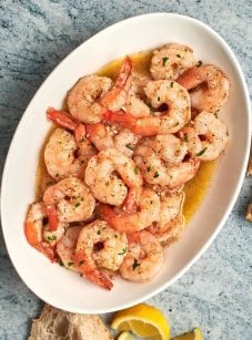 garlic butter shrimp on platter with bread and lemon wedges.