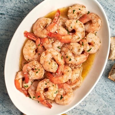 garlic butter shrimp on platter with bread and lemon wedges.