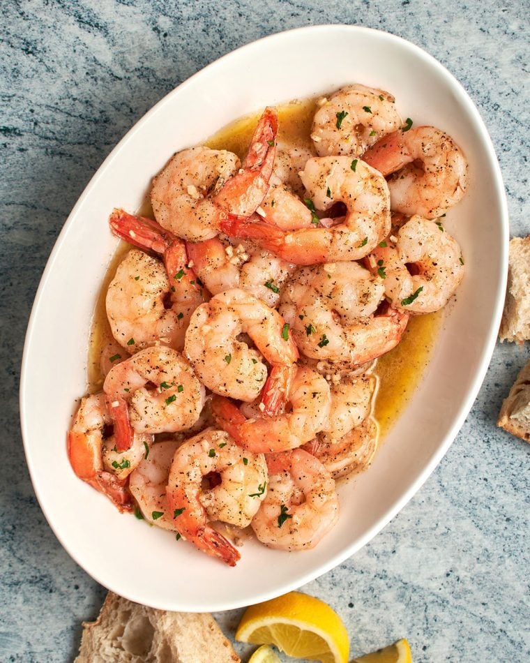 garlic butter shrimp on platter with bread and lemon wedges.