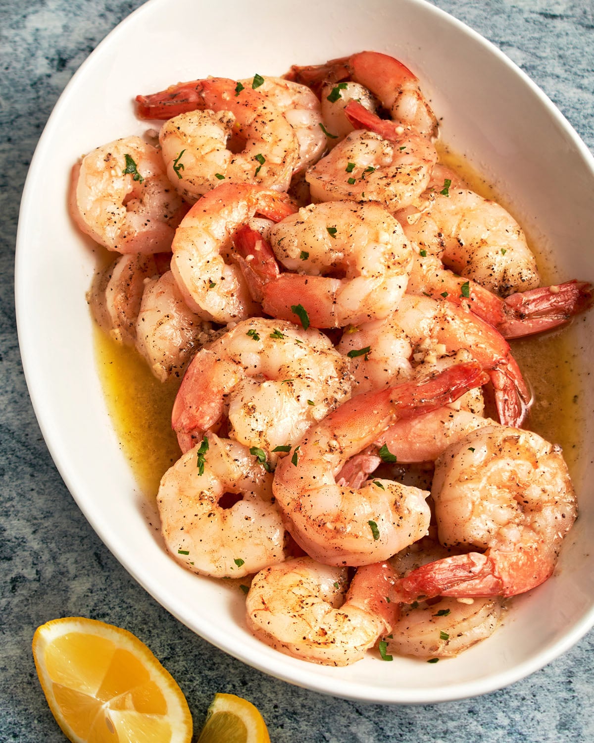garlic butter shrimp on platter with lemon wedges.