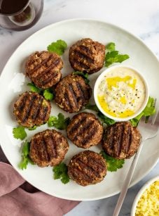 Grilled Moroccan meatballs with yogurt sauce on white platter.