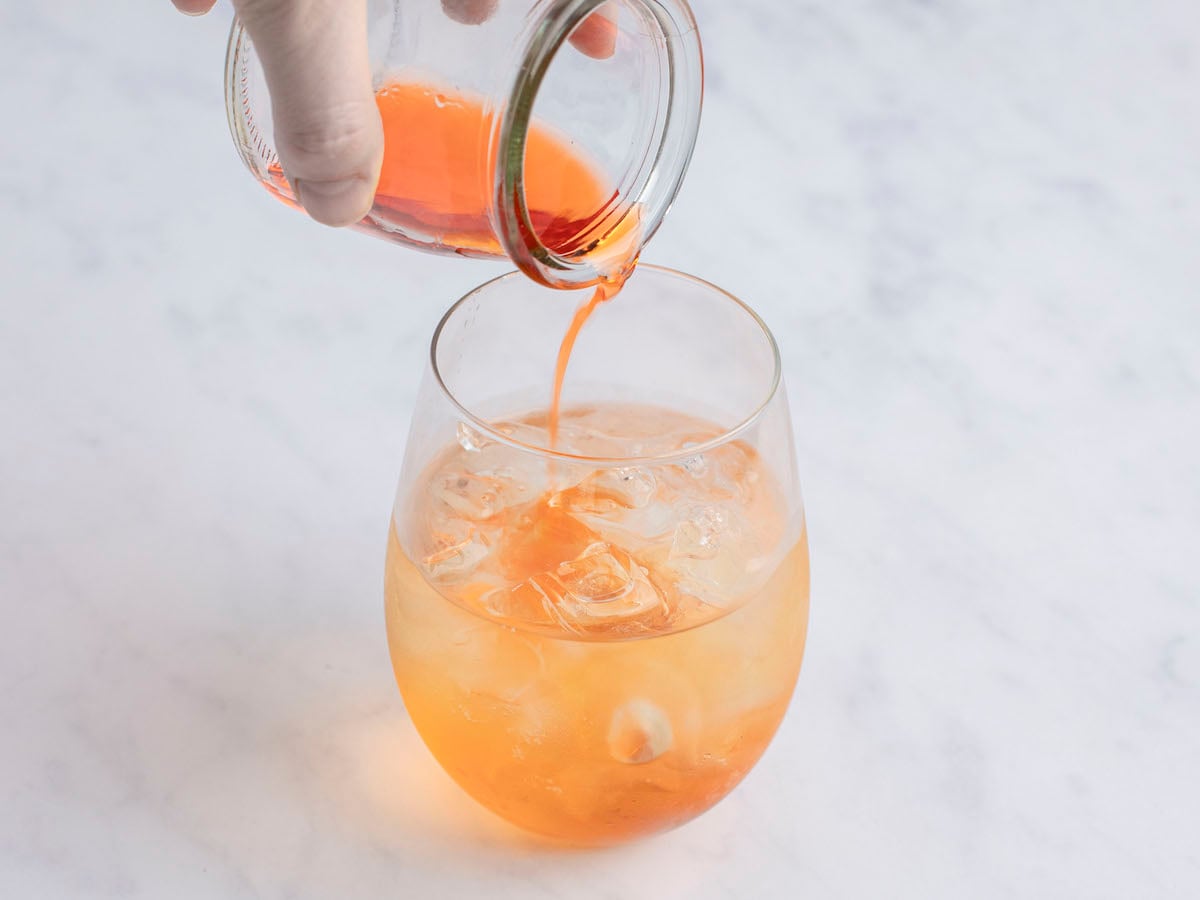 adding aperol into large wine glass with ice cubes and Prosecco