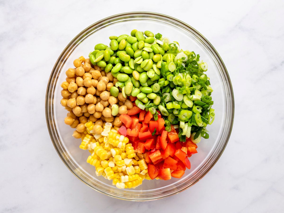 chickpeas, red pepper, corn kernels, edamame, and scallions in separate piles in large glass bowl