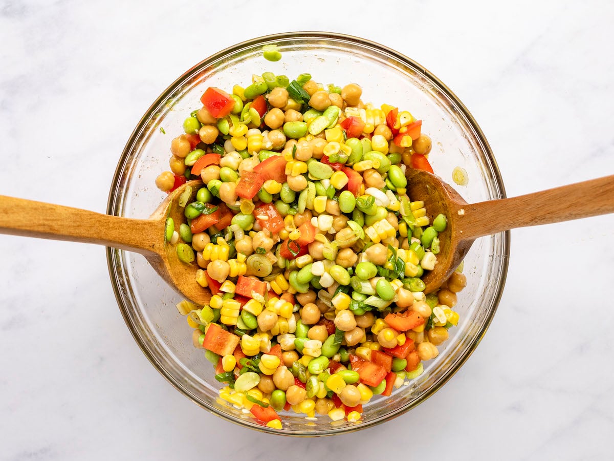 all salad ingredients mixed together with two large wooden spoons in bowl