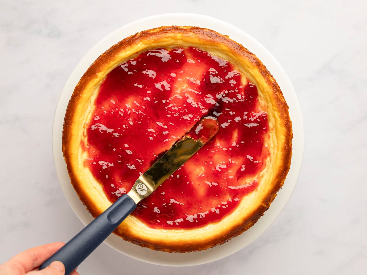 spreading jam over ricotta cheesecake