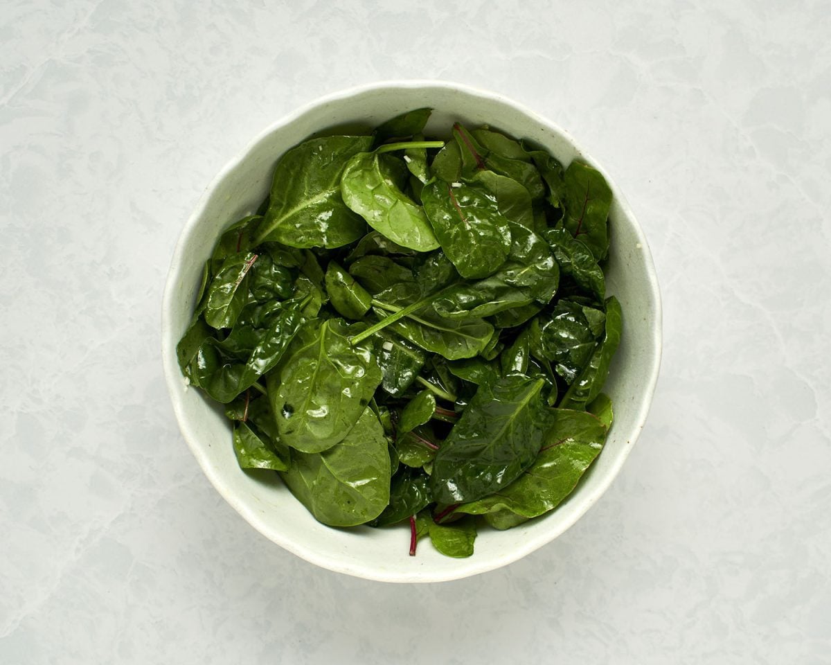 mixed greens tossed with salad dressing in white bowl