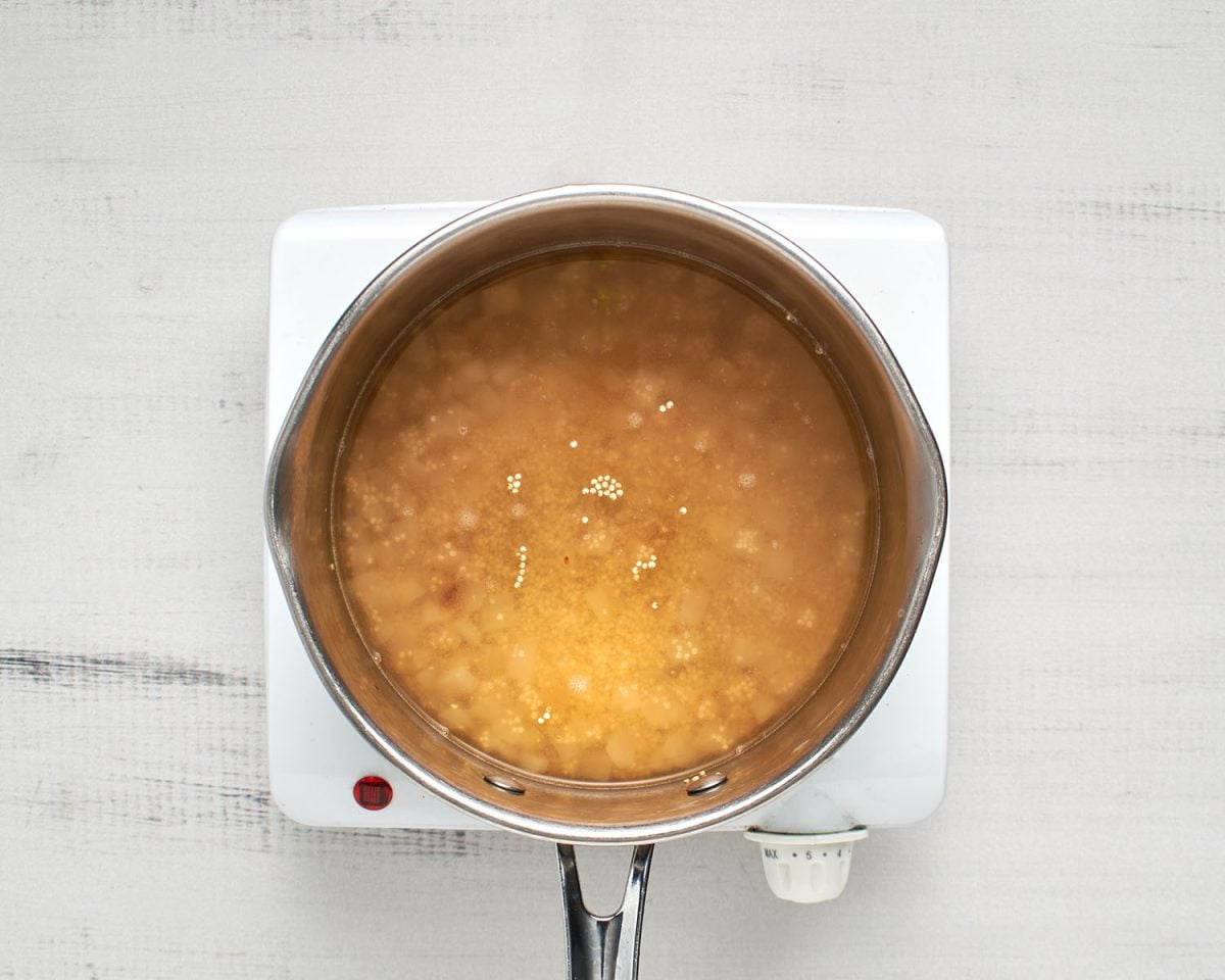 quinoa and vegetable broth in saucepan with cooked onions