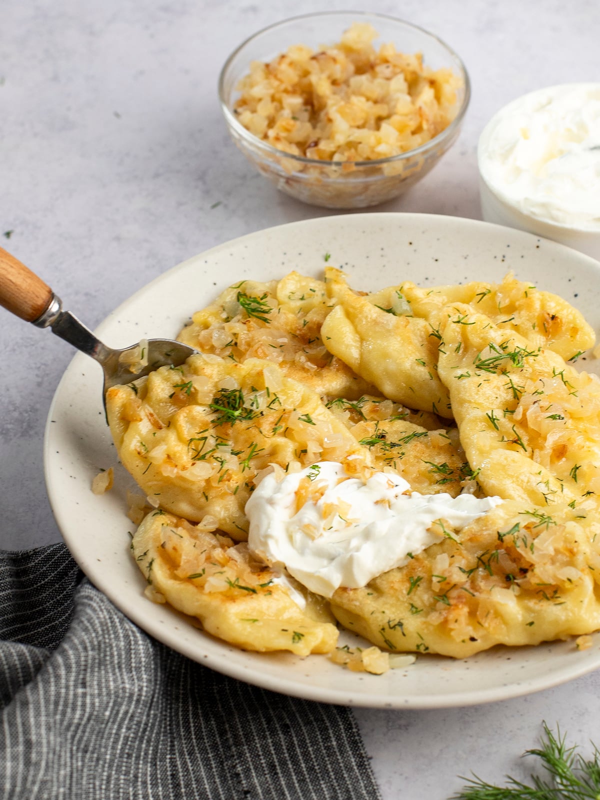 cooked pierogies on large white plate topped with dollop of sour cream
