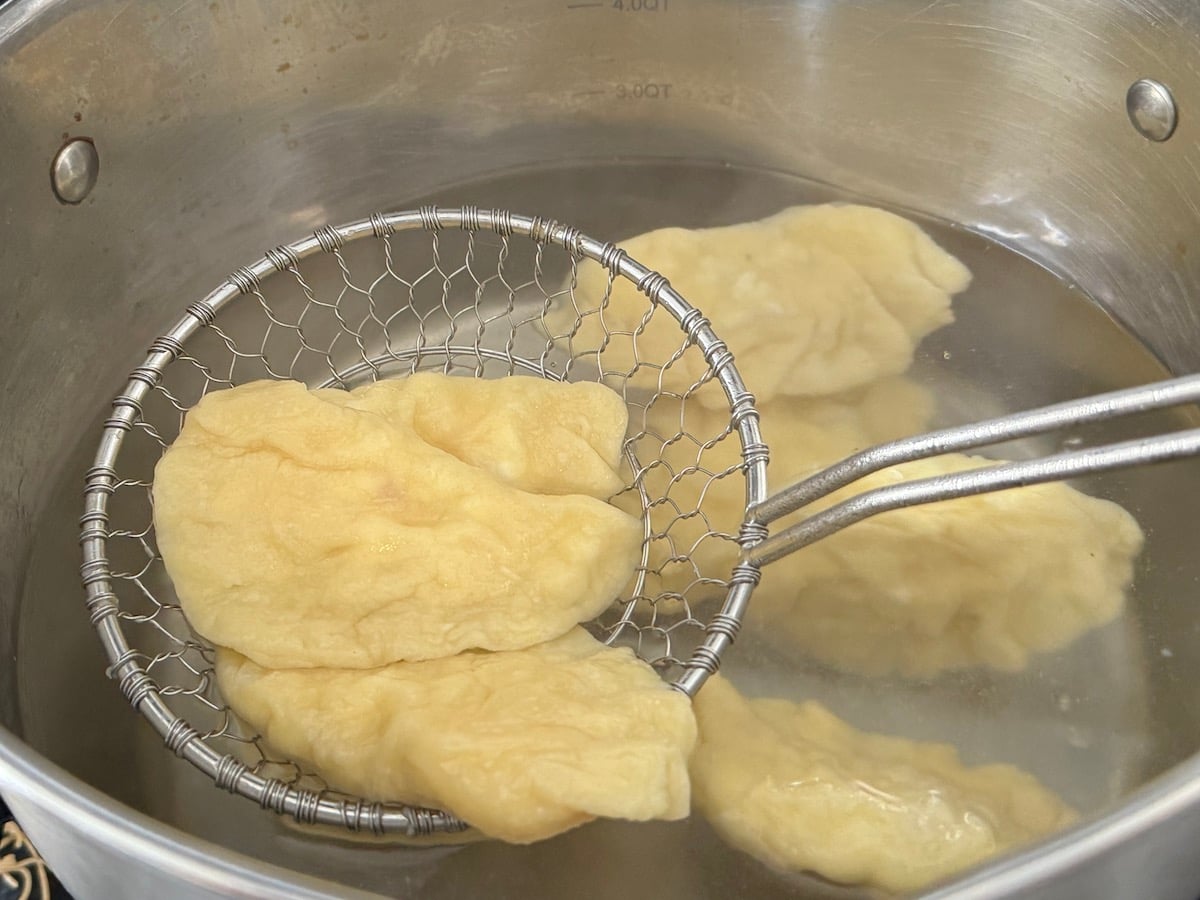 spider strainer removing 3 pierogi from pot filled with boiling water