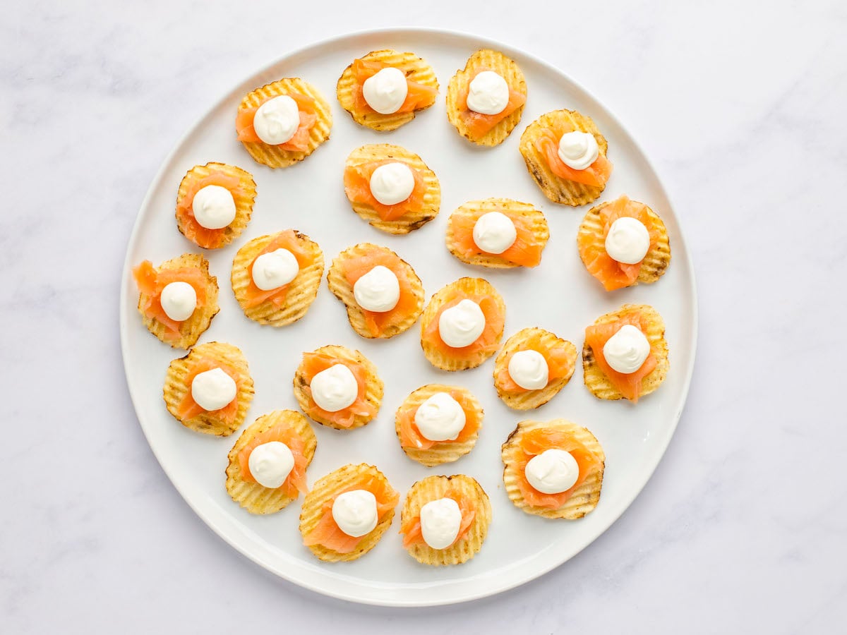 potato chips on white serving plattered topped with smoked salmon and dollop of cream cheese mixture