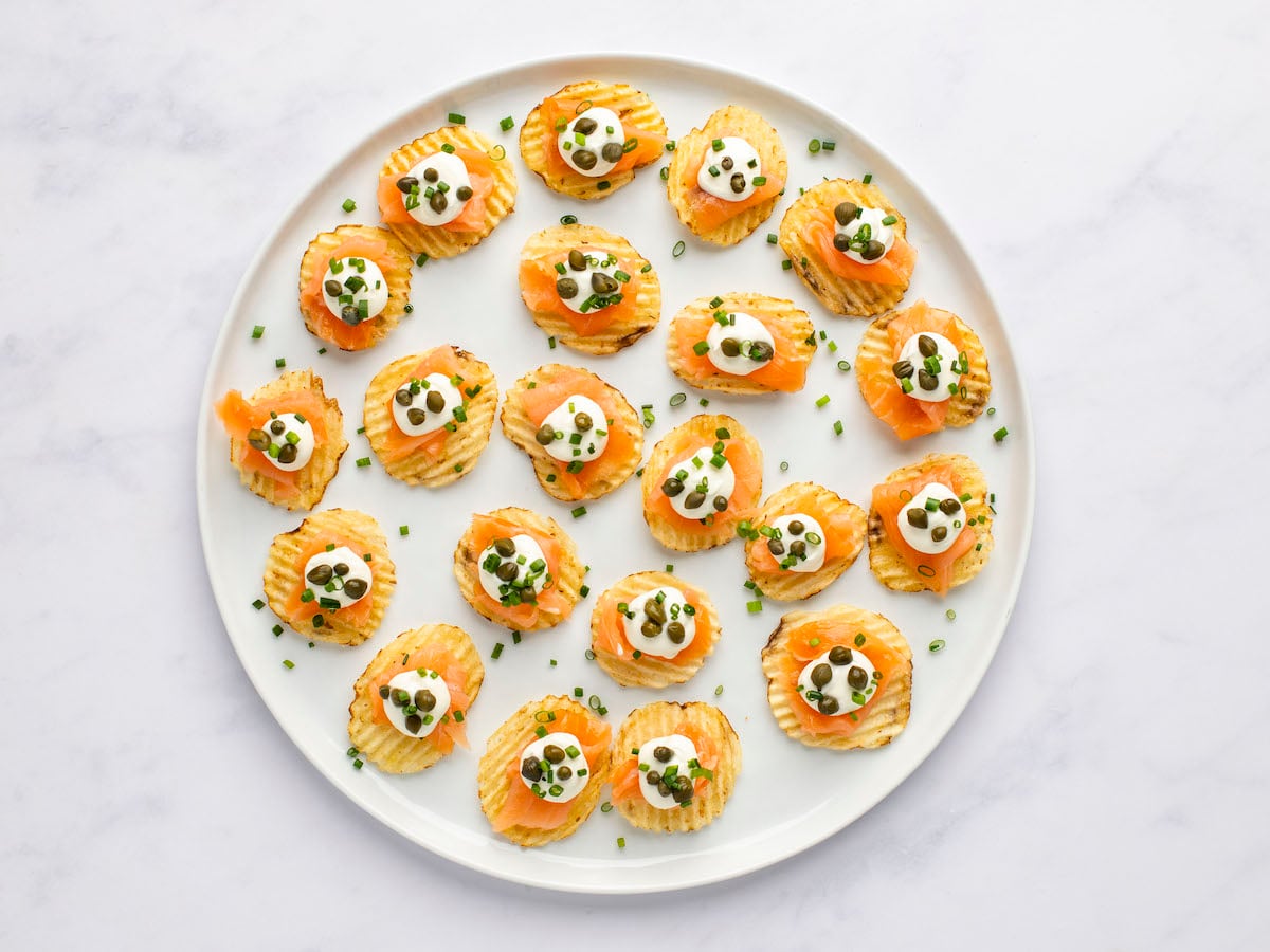 potato chips on white serving plate topped with smoked salmon, cream cheese mixture, capers and chives