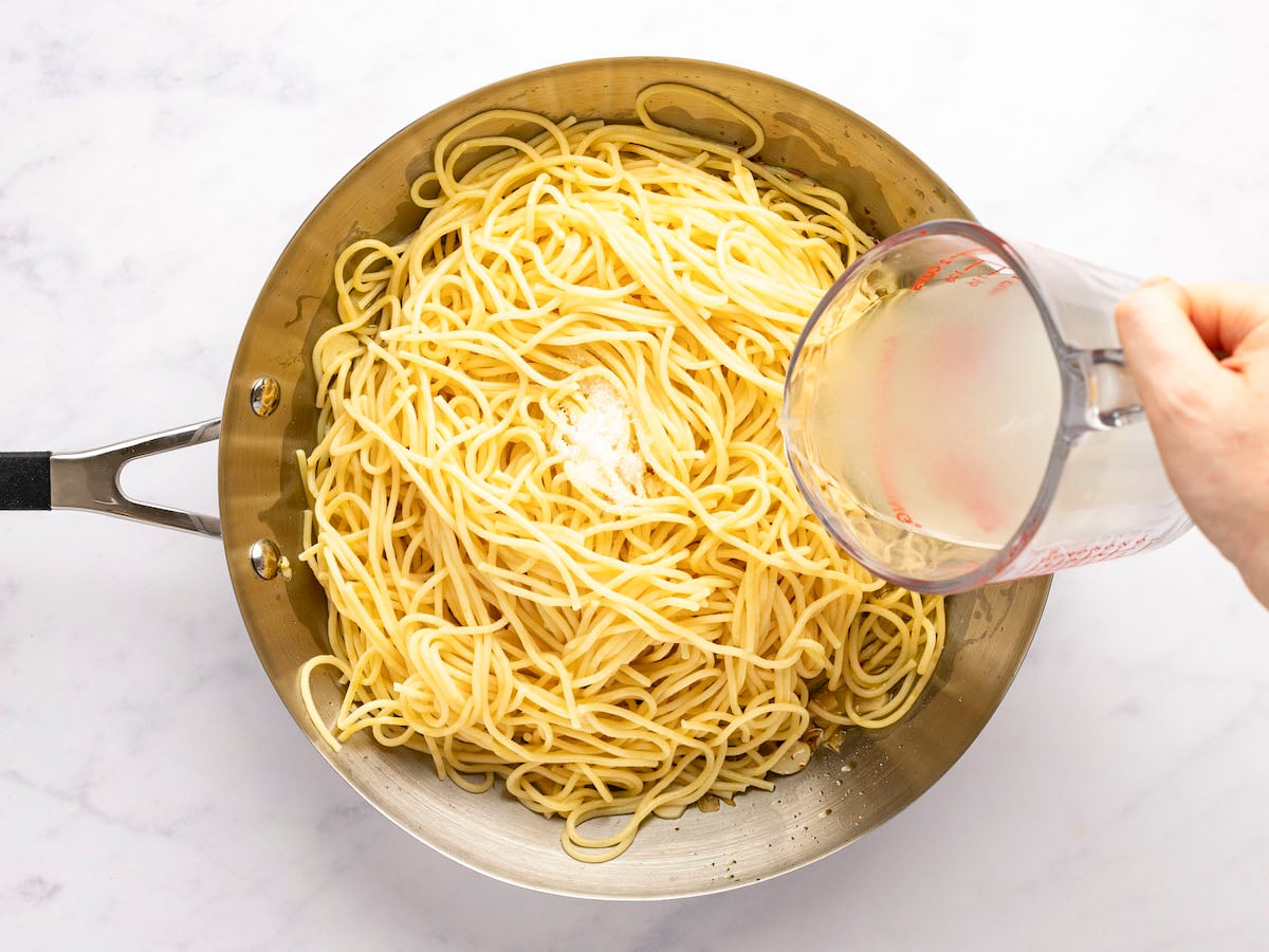 pouring 3/4 cup pasta cooking liquid into skillet with spaghetti