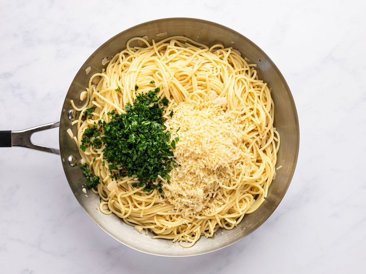 large skillet with chopped parsley and cheese piled on top of cooked pasta