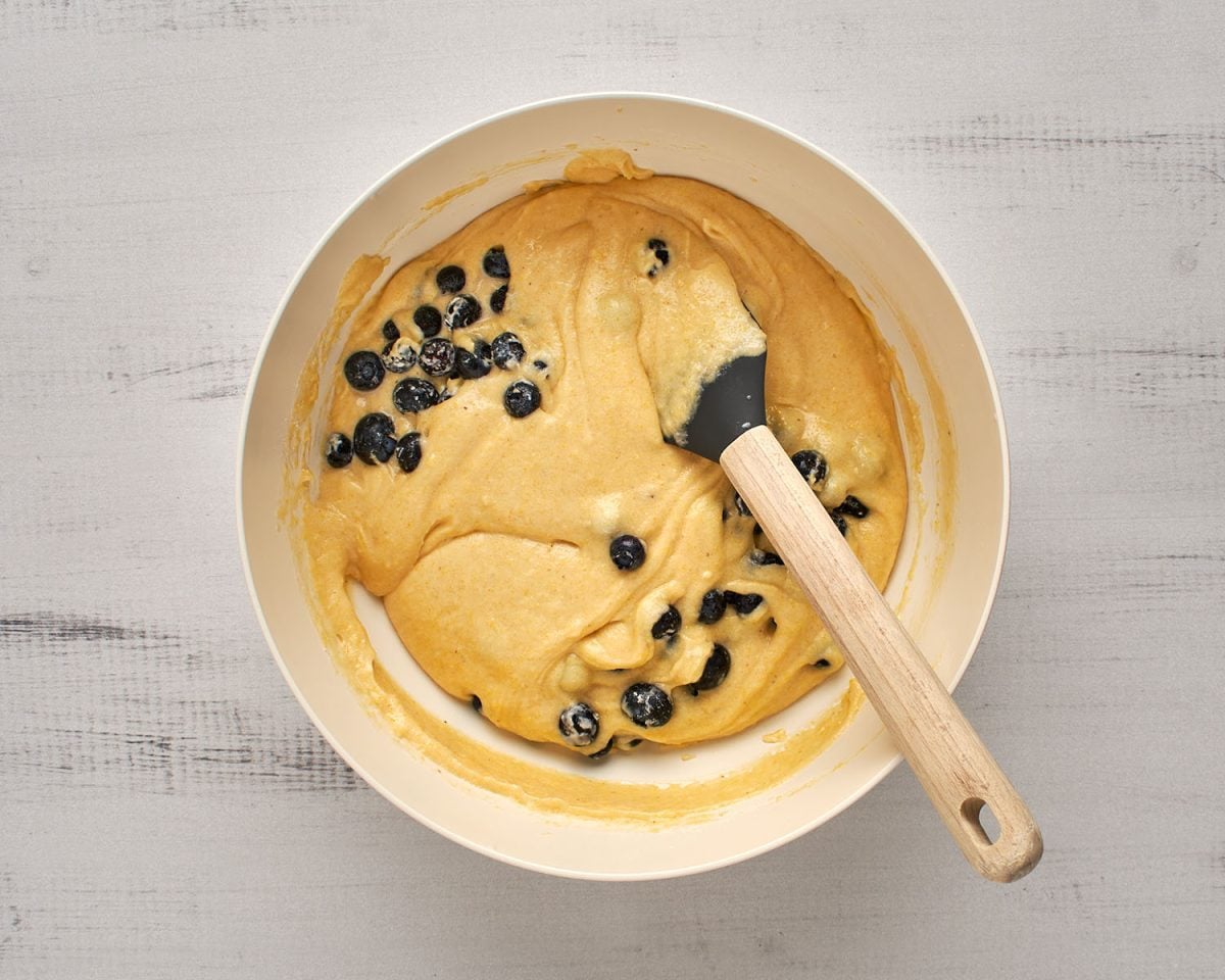 stirring blueberries into batter in large white mixing bowl