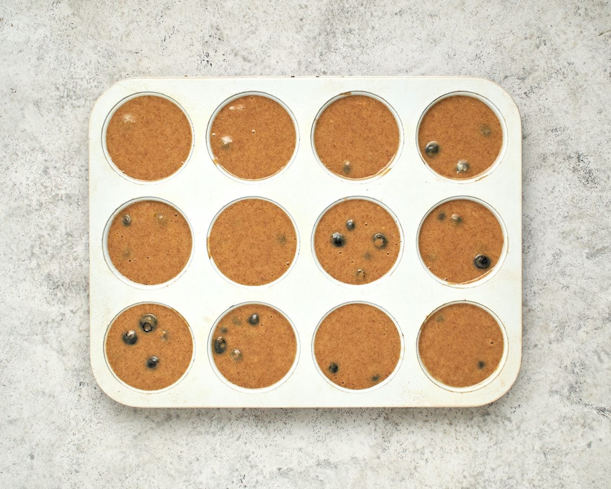 muffin tin filled with bluberry muffin batter