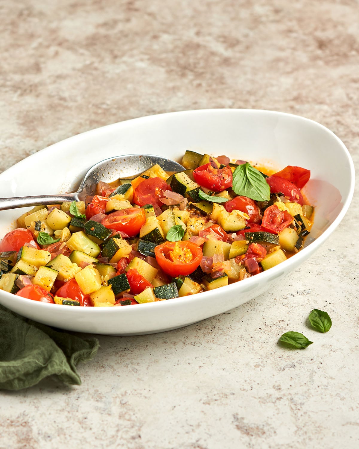 Sautéed Zucchini and Cherry Tomatoes in white oval serving dish with spoon protruding