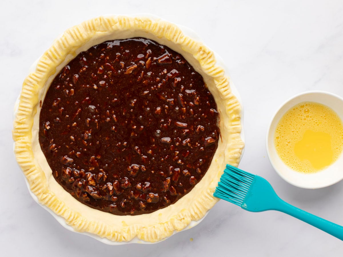 filling in pie crust and brush brushing beaten egg on crust edges