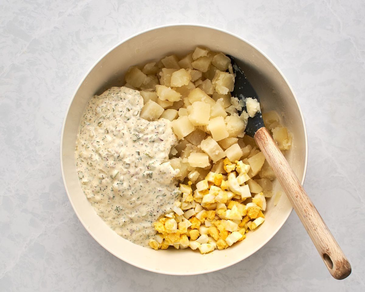 cooked potatoes and diced eggs added to white bowl with dressing