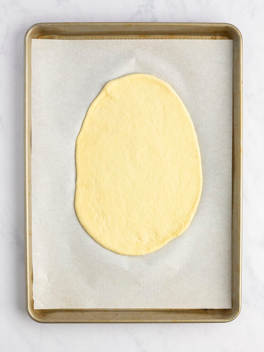 parchment-lined baking sheet with dough ball rolled into oval
