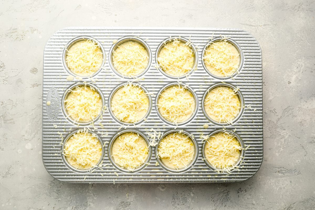 popover batter with cheese sprinkled on top in muffin tin