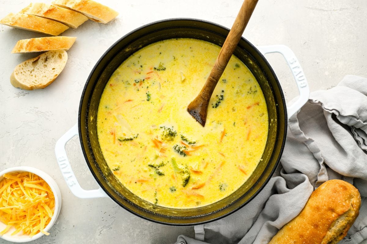 broccoli cheddar soup in Dutch oven with cheddar cheese and bread on the side.