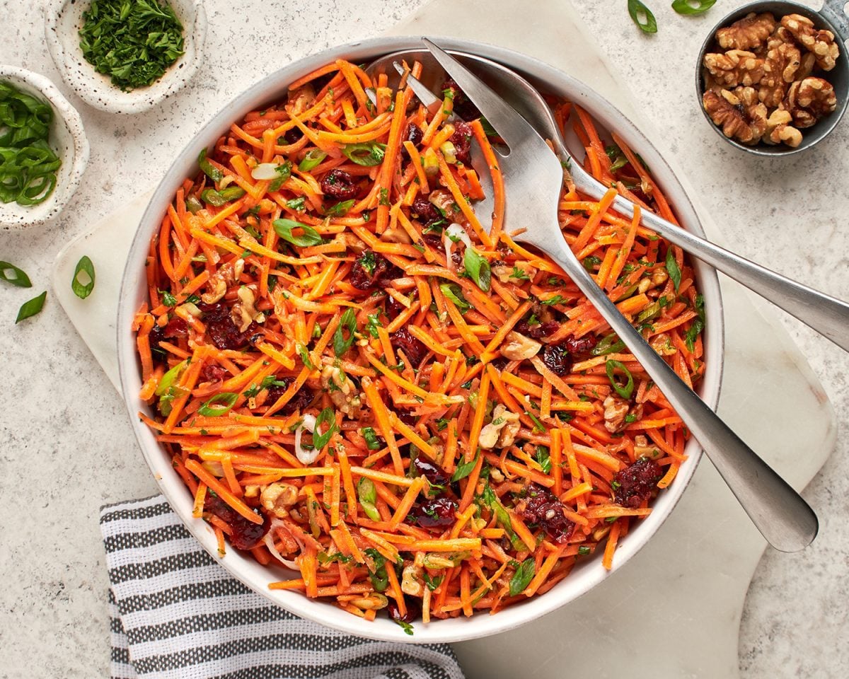 bowl of carrot slaw with cranberries and walnuts with cloth napkin