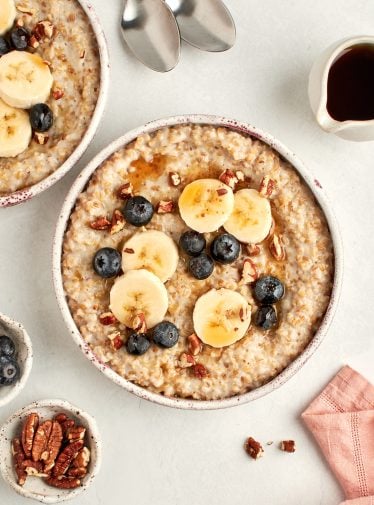 bowls of steel cut oats topped with blueberries, bananas, pecans and maple syrup