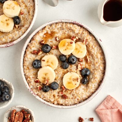 bowls of steel cut oats topped with blueberries, bananas, pecans and maple syrup