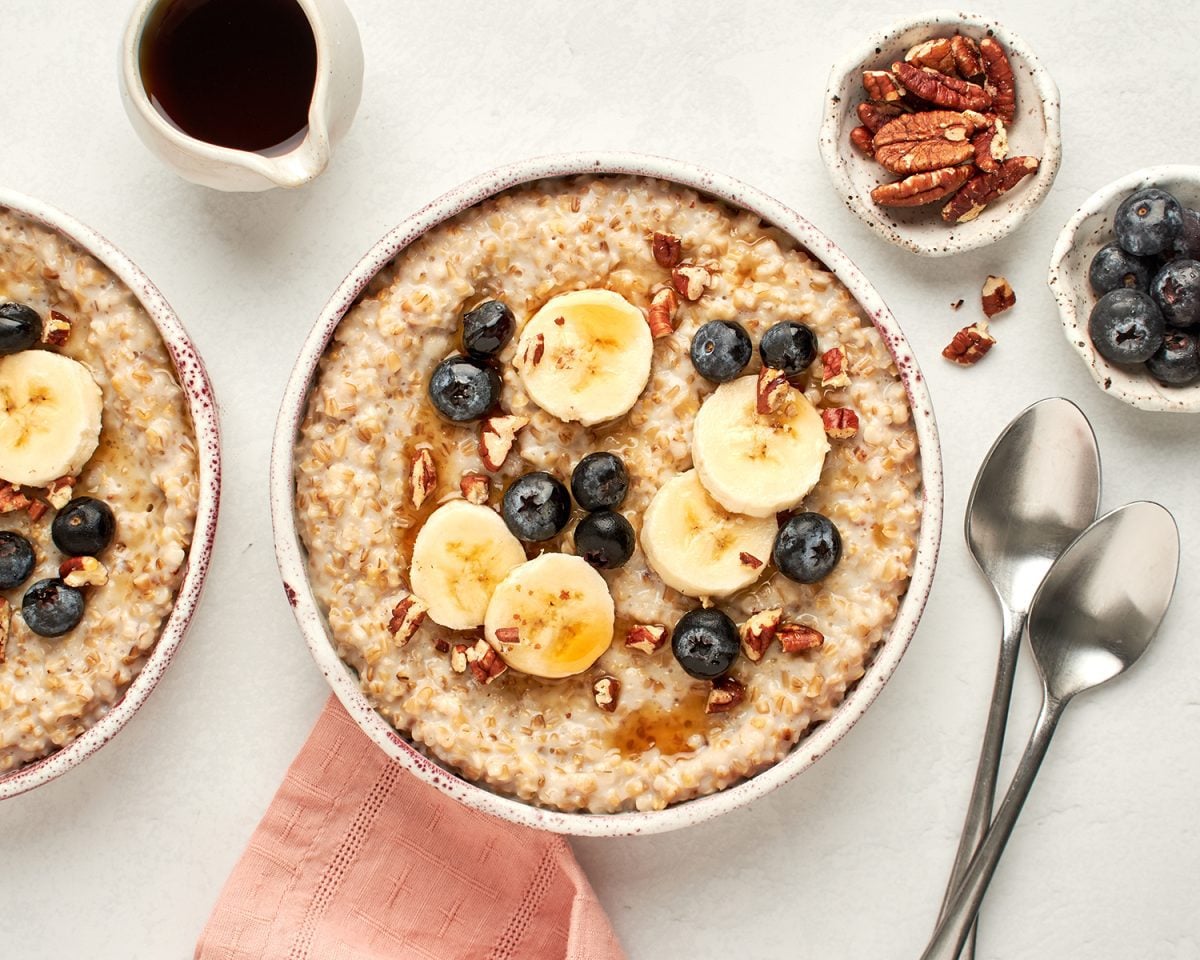 bowls of creamy steel cut oats with maple syrup, bananas, blueberries and pecans
