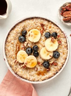 bowls of creamy steel cut oats with maple syrup, bananas, blueberries and pecans