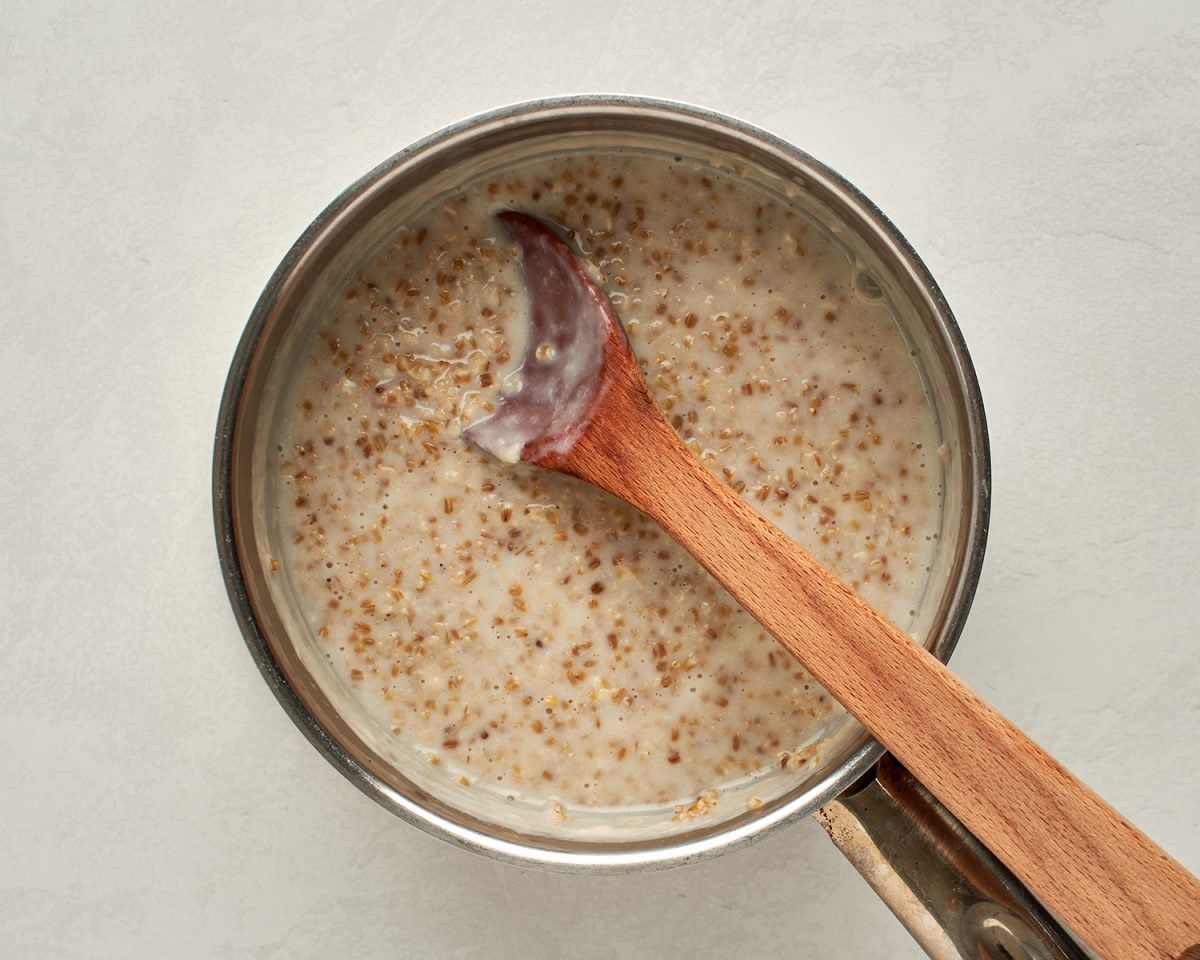 cooked steel cut oats in pan with wooden spoon