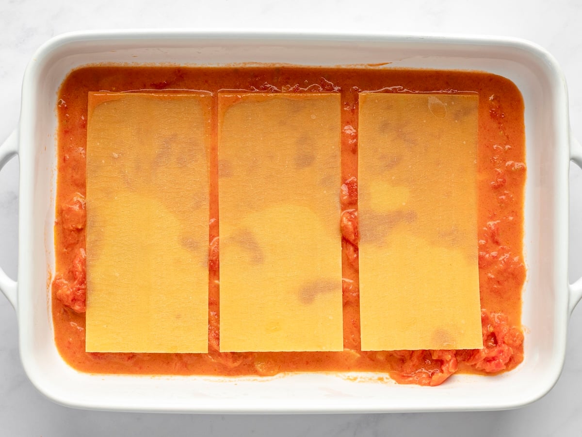 layering cheese lasagna with sauce and noodles.