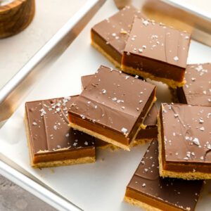millionaire's shortbread bars on baking sheet with bowl of flaky sea salt.