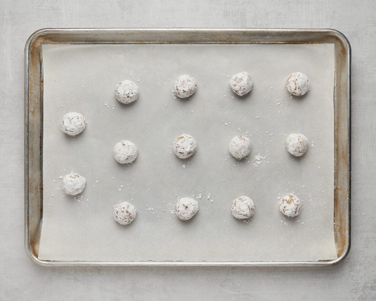 confectioner sugar-covered dough balls on parchment-lined baking sheet