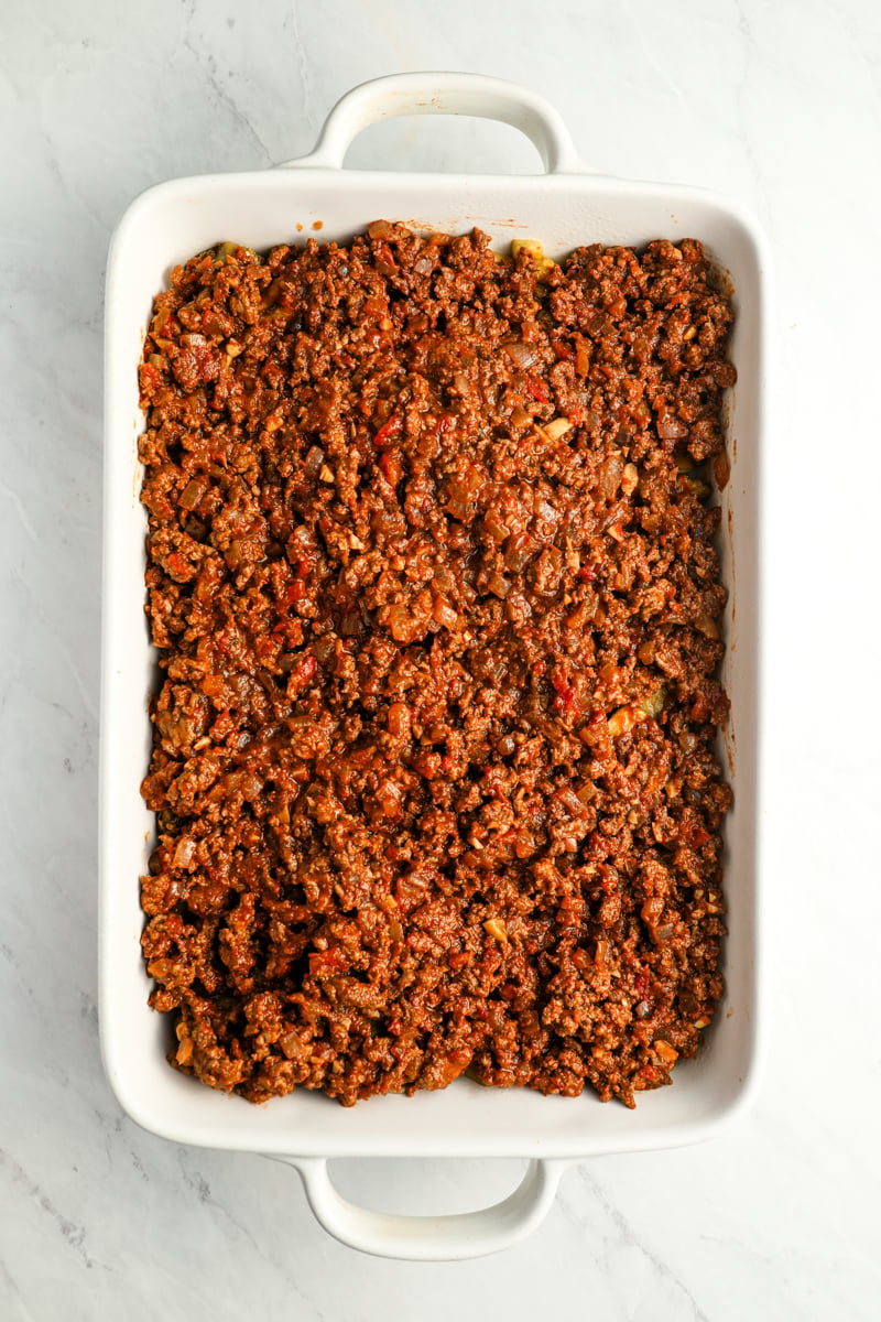 meat sauce spread over vegetables in baking dish
