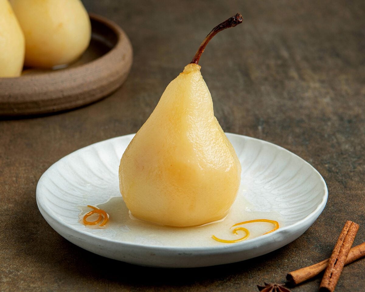 poached pear garnished with citrus peels on white plate with syrup