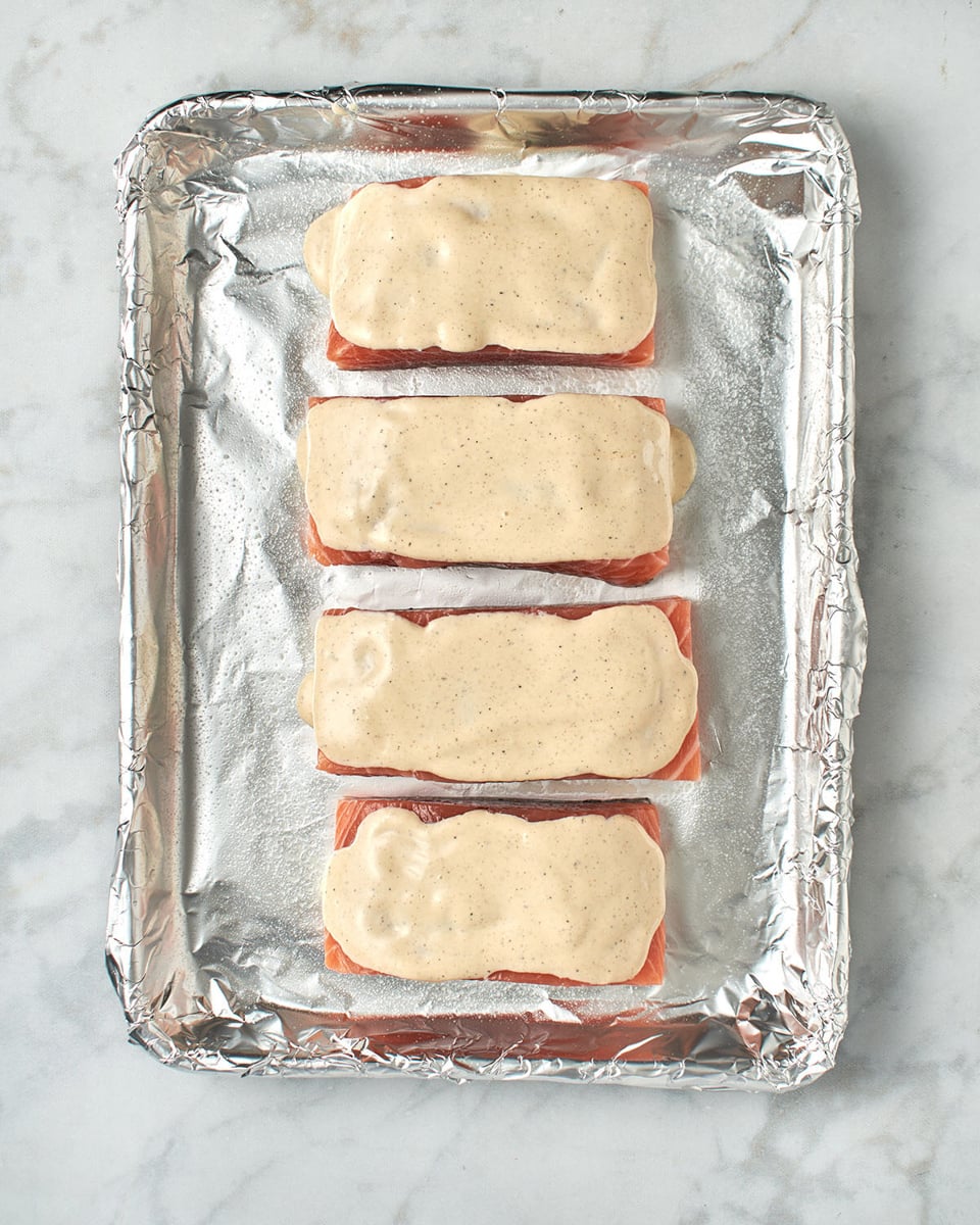 salmon topped with sauce on baking sheet.
