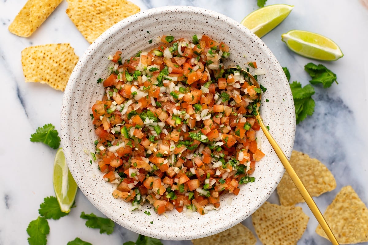 pico de Gallo in white bowl with tortilla chips and limes scattered around bowl